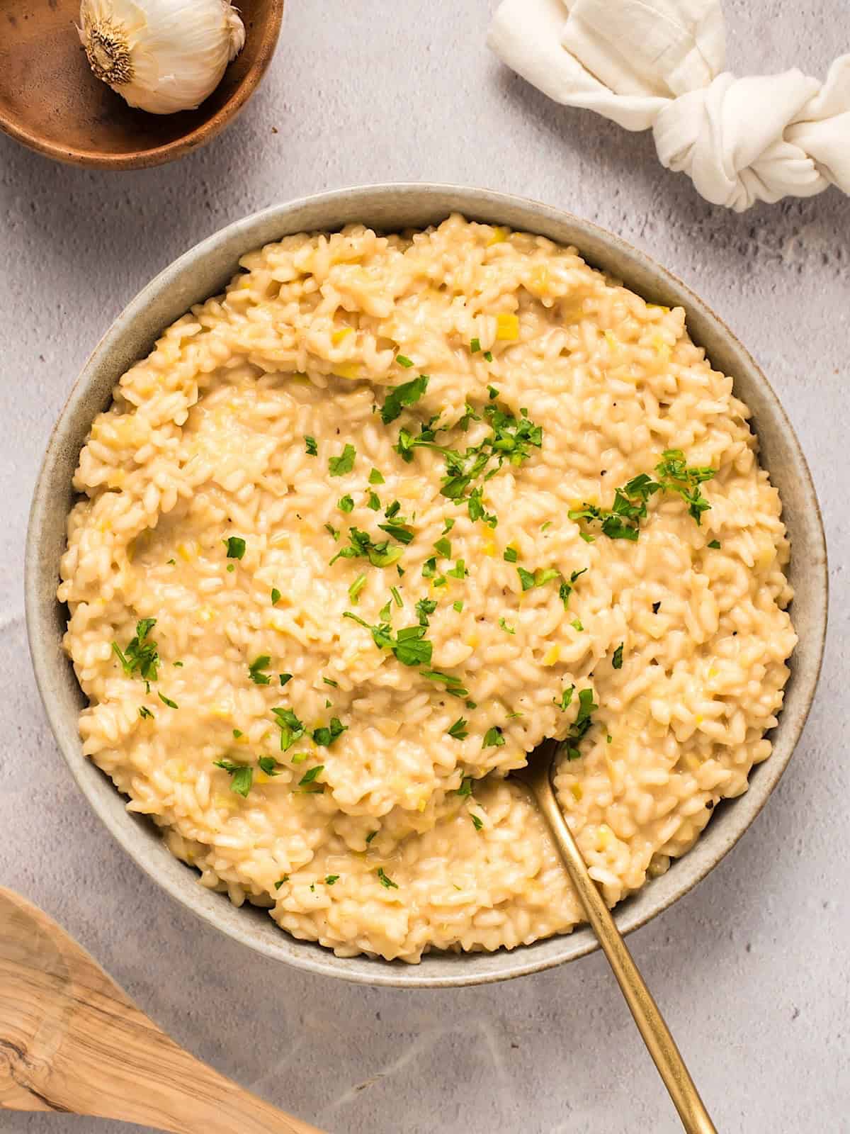 Roasted garlic and leek risotto plated near linen, garlic bulb, and wooden spoon.