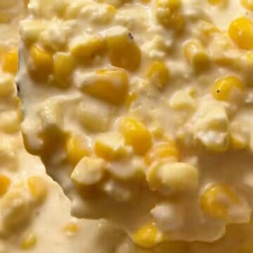 A ladle of creamed corn above the slow cooker showing the creamy texture.