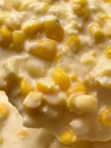 A ladle of creamed corn above the slow cooker showing the creamy texture.