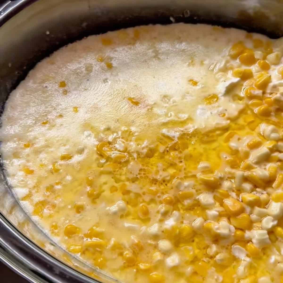 Melted butter on top of slow cooker shows corn cooked halfway through before stirring.