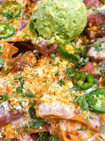 Steak elote nachos on a sheet pan with queso and guacamole.