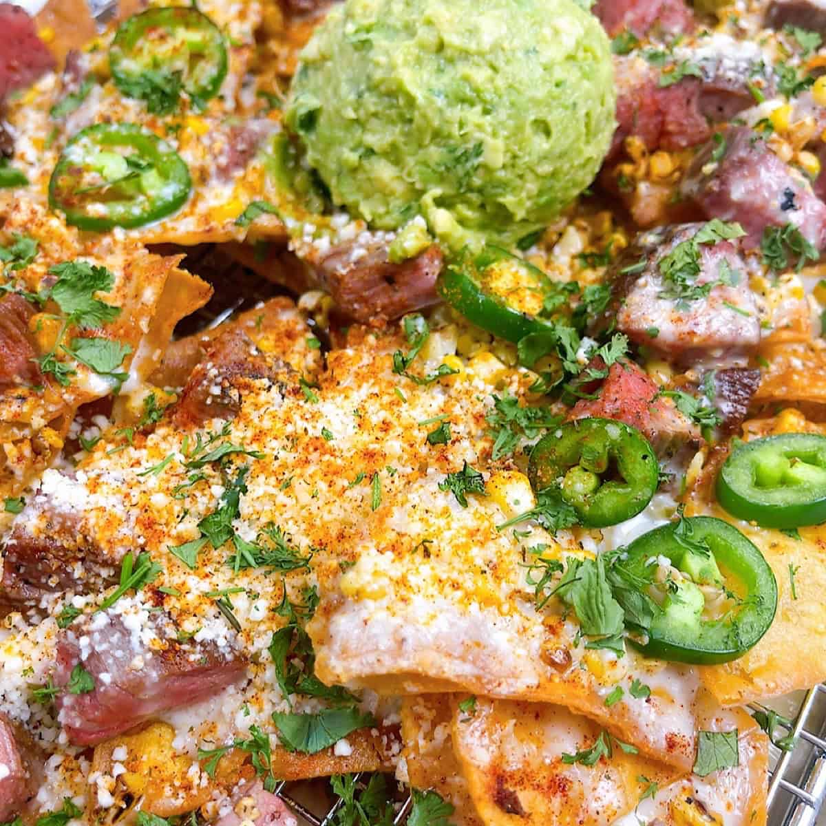 Steak elote nachos on a sheet pan with queso and guacamole.