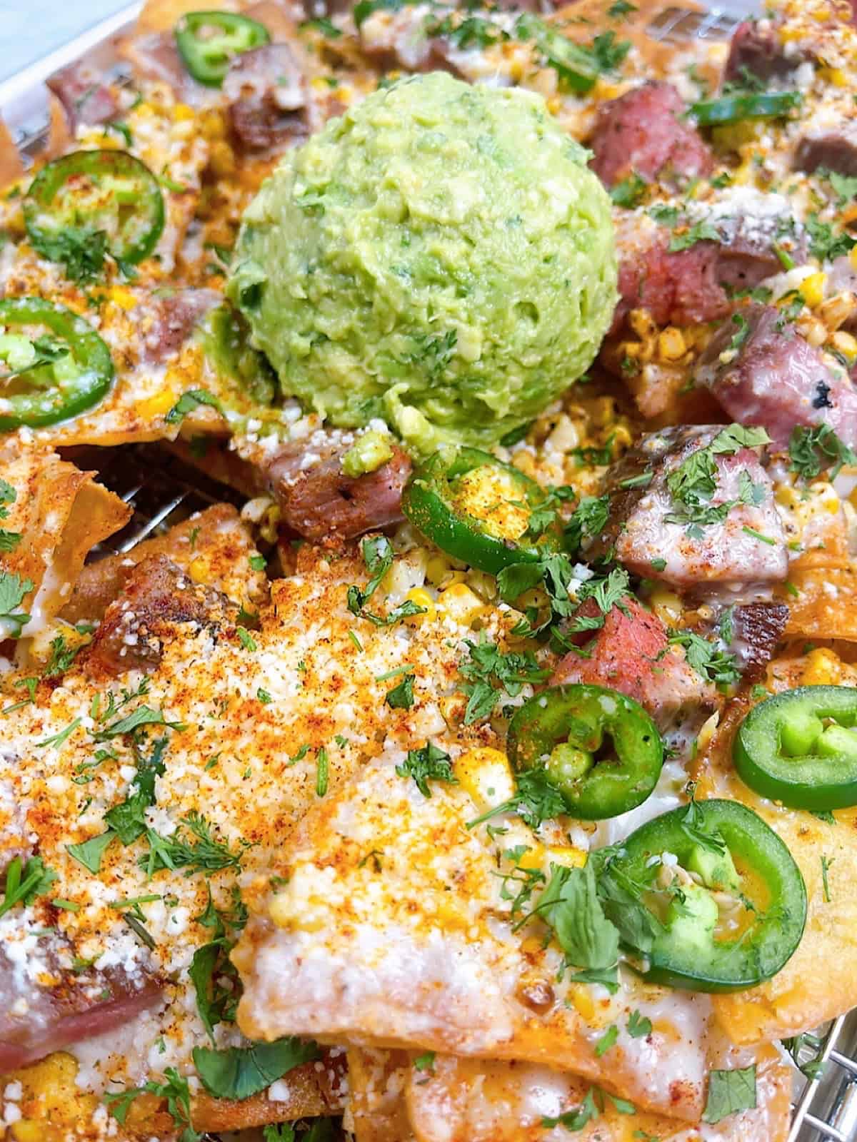 Steak elote nachos on a sheet pan with queso and guacamole.