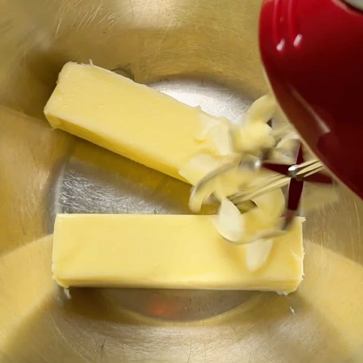 Two sticks of softened butter in a mixing bowl with beaters showing consistency.