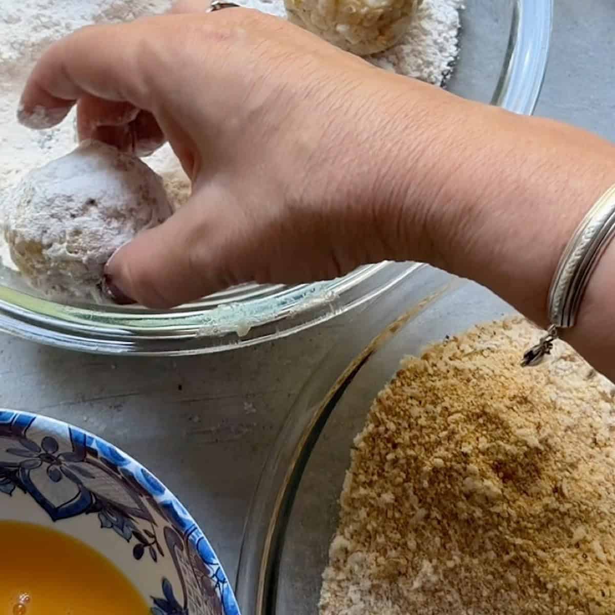 A breading station with an arancini ball being lightly rolled into flour.