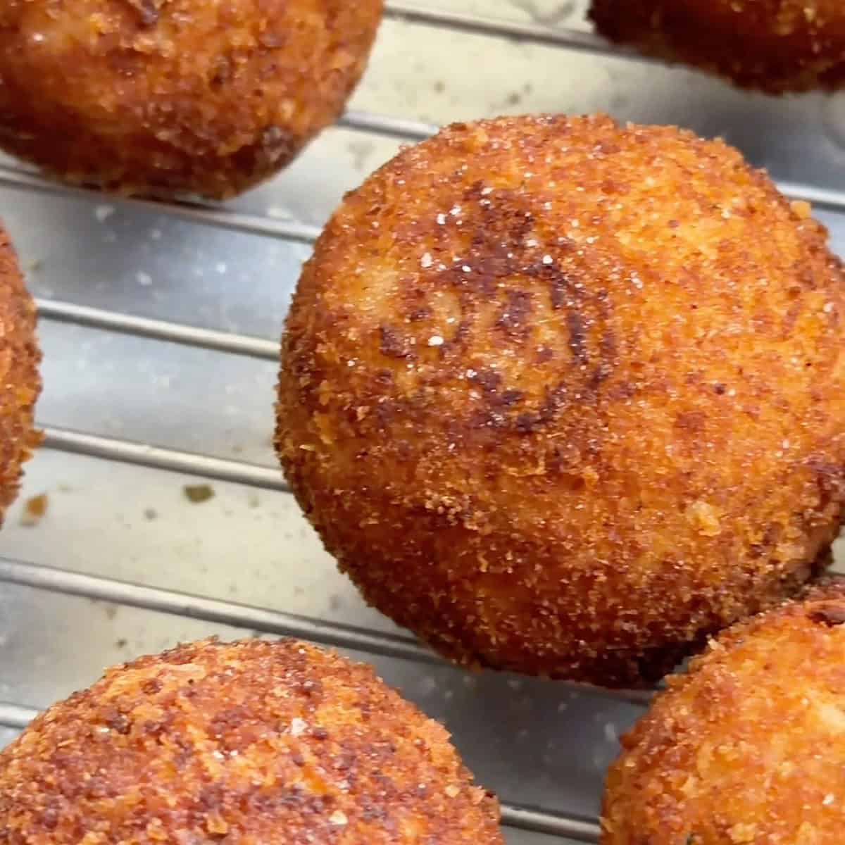 Fried arancini draining on a wire rack.