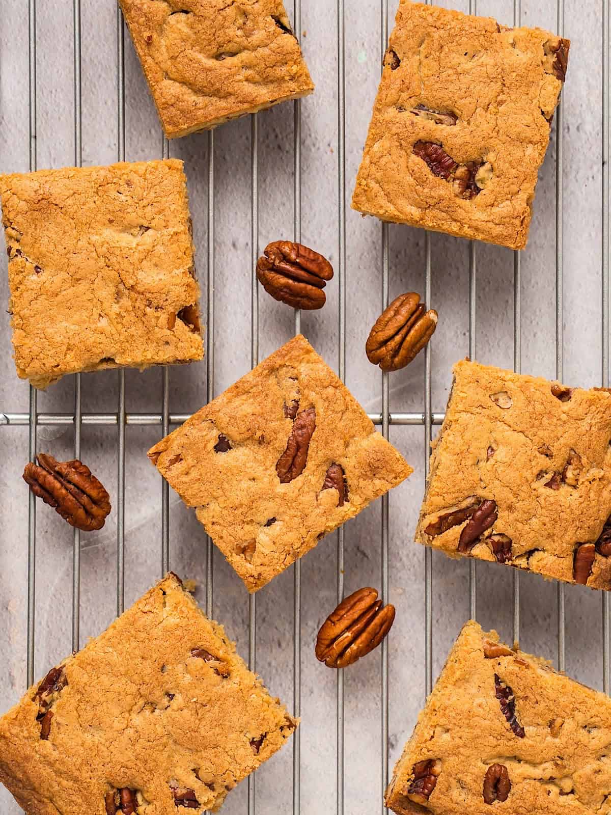 Golden brown butter pecan blondies on a cooling rack with pecans.
