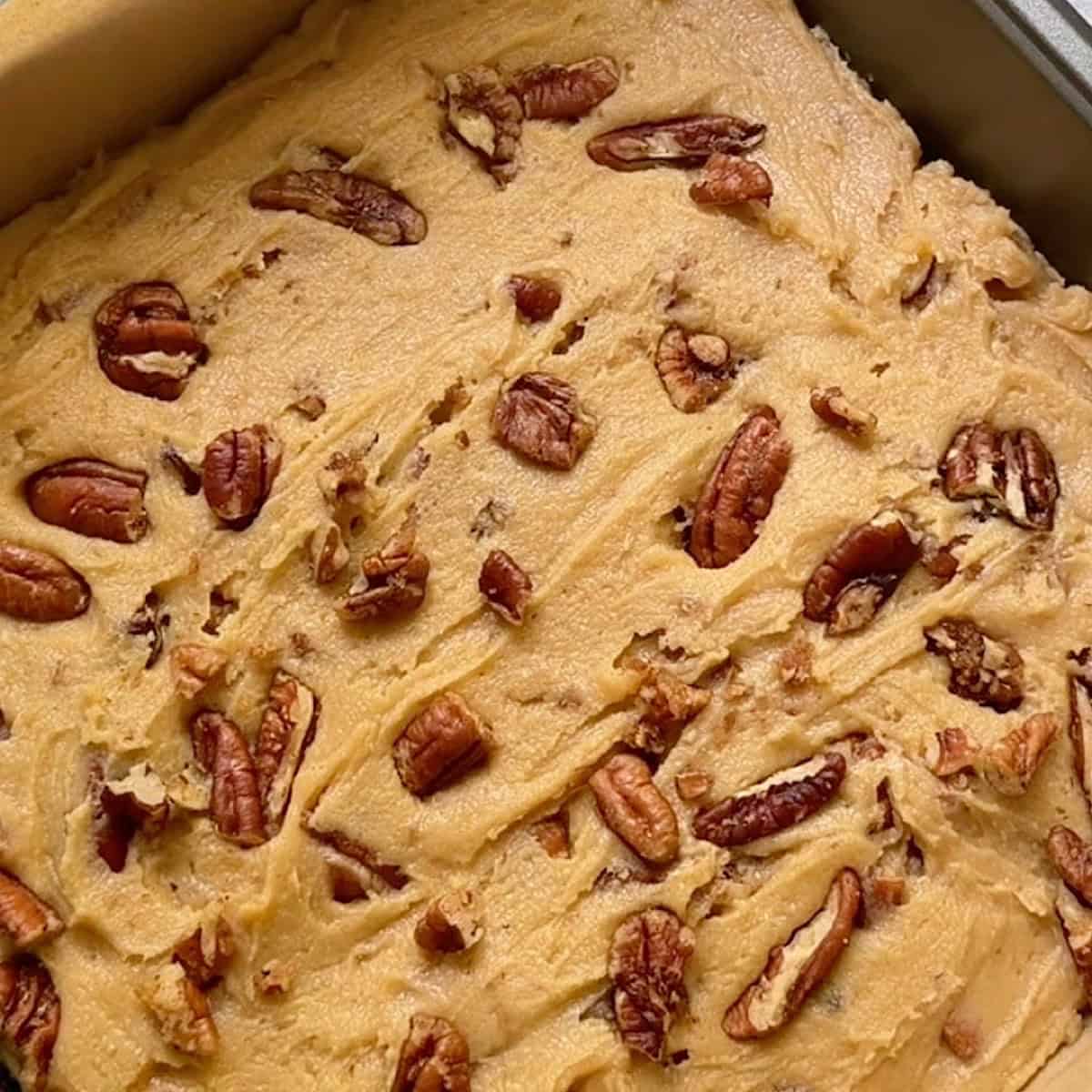 Batter spread into a baking dish and topped with pecan pieces.