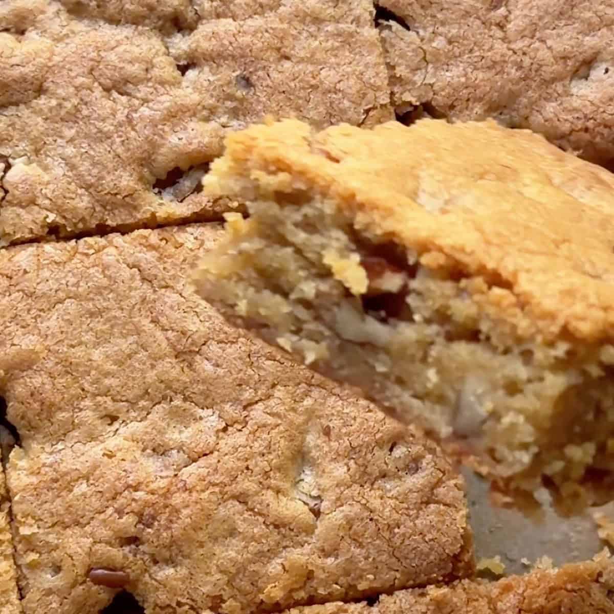 Holding a blondie slice above baking pan to show chewy middle.