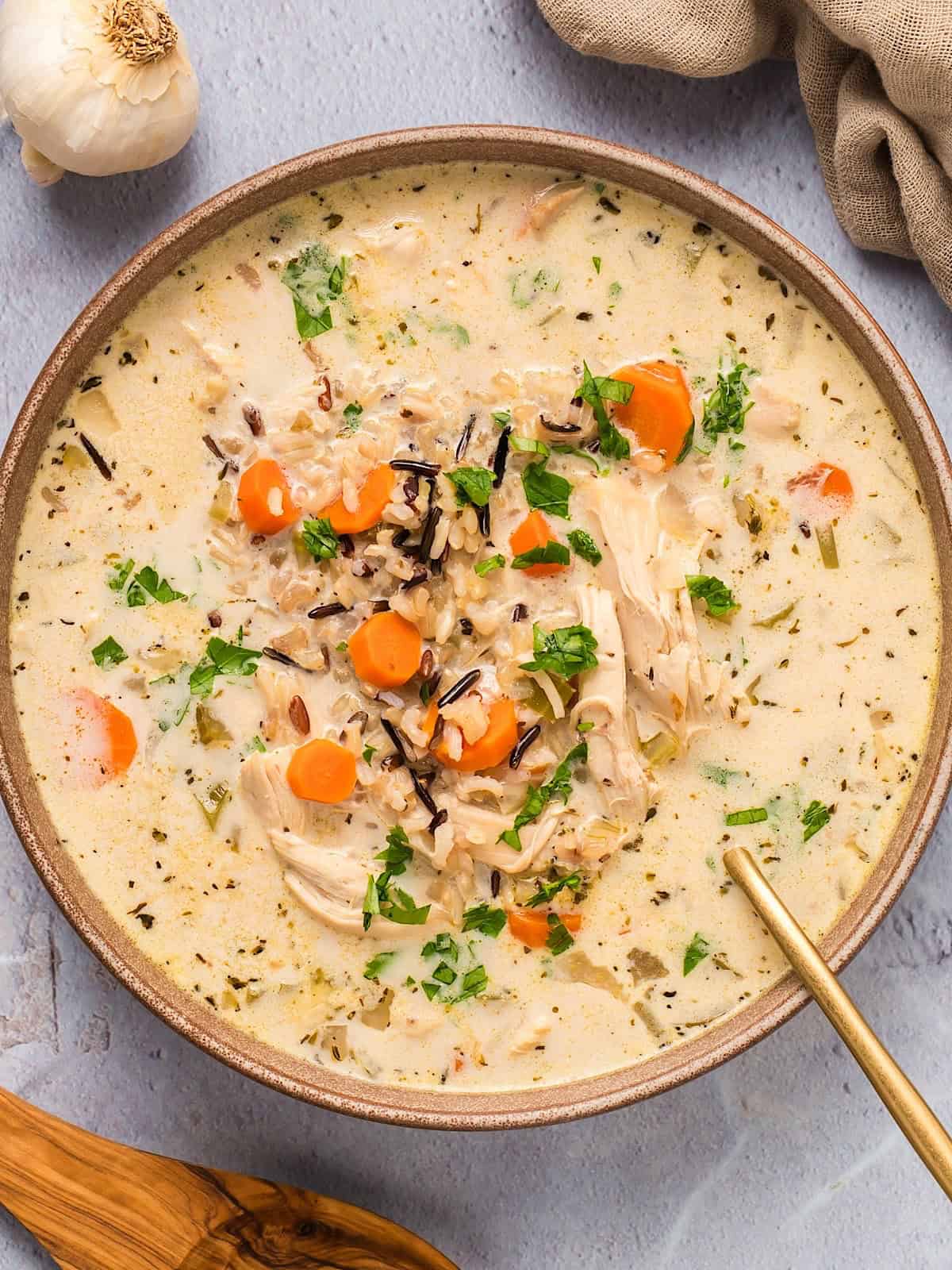 Creamy chicken and wild rice soup with herbs in a brown bowl.