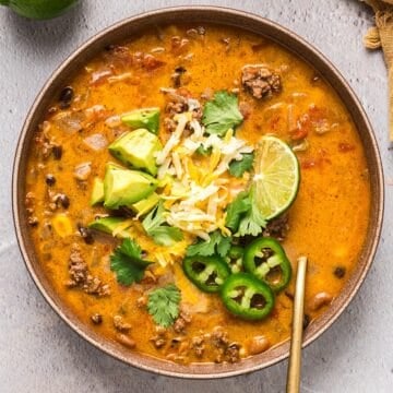 A wide shallow bowl fo creamy ground beef taco soup with avocado, cilantro, lime, and jalapeno garnish.