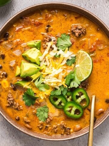 A wide shallow bowl fo creamy ground beef taco soup with avocado, cilantro, lime, and jalapeno garnish.