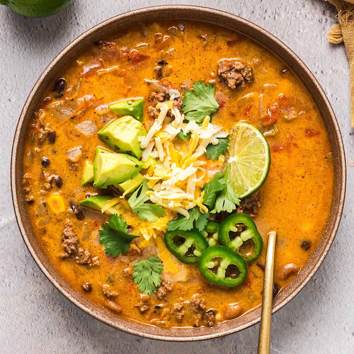 A wide shallow bowl fo creamy ground beef taco soup with avocado, cilantro, lime, and jalapeno garnish.