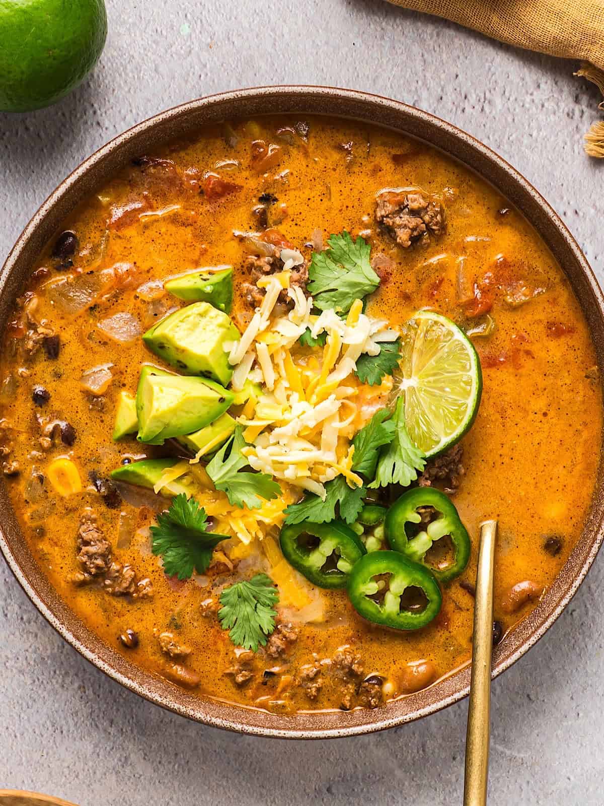 A wide shallow bowl fo creamy ground beef taco soup with avocado, cilantro, lime, and jalapeno garnish.