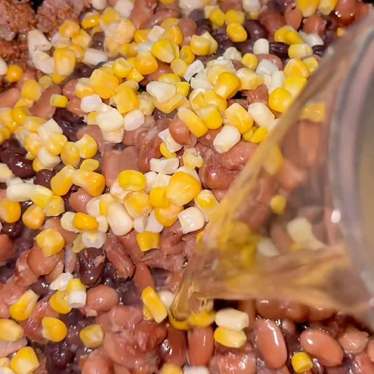 Adding chicken broth to the tomato base with beans and corn.