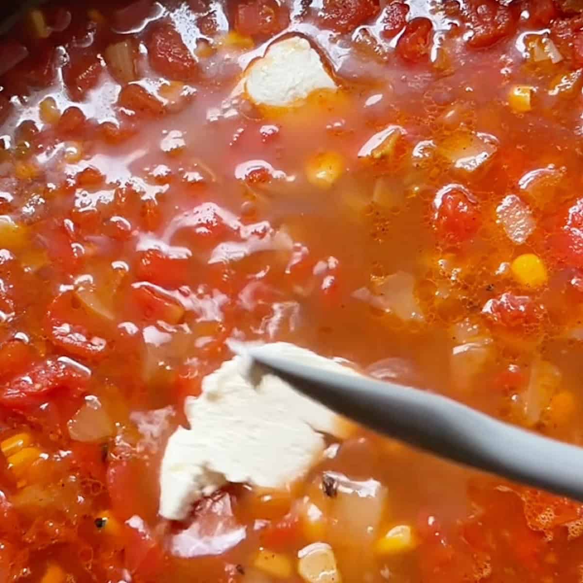 Simmering ground beef taco soup with cream cheese being stirred into the broth.