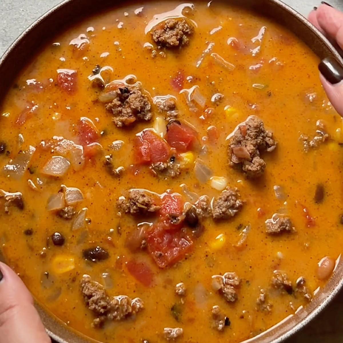 Ladled creamy ground beef taco soup into bowl ready for toppings.