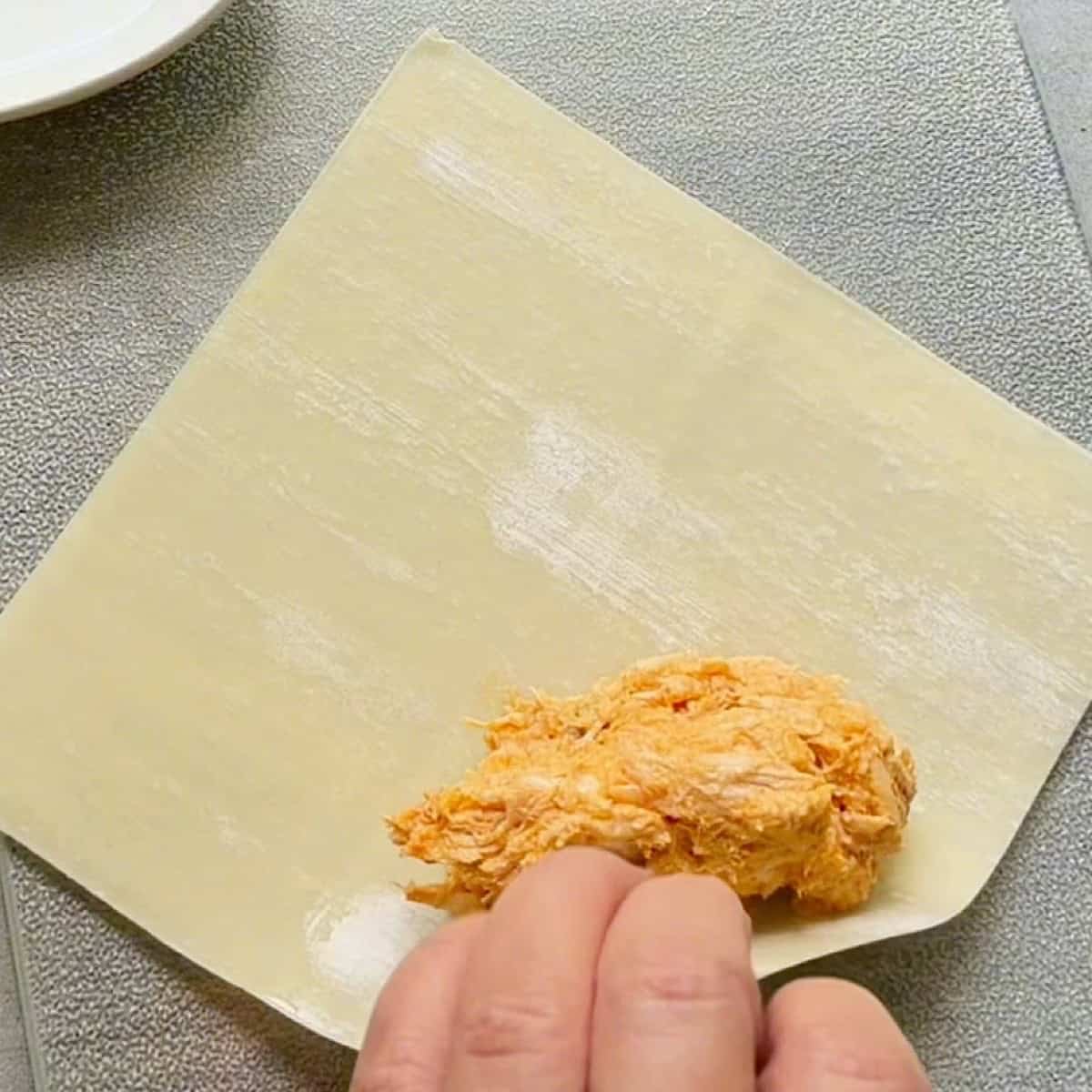 Rolling up the egg roll wrapper with filling from a diagonal corner.