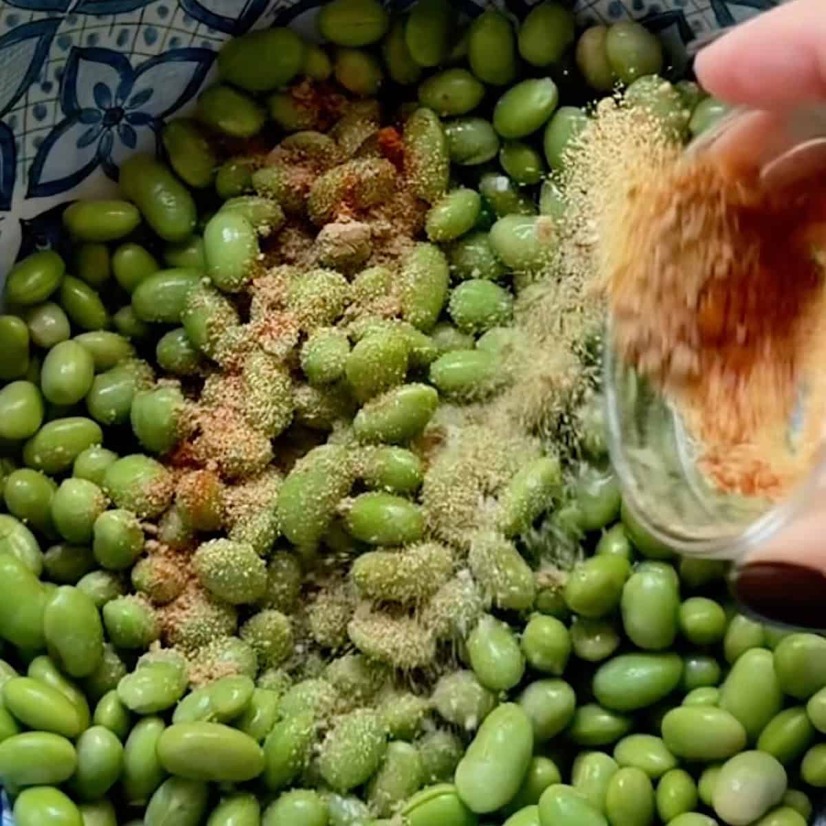 Sprinkling seasoning over the edamame in a bowl.