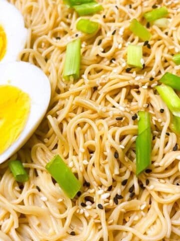 Garlic ginger ramen in a black bowl with sesame garnish and hard boiled eggs.