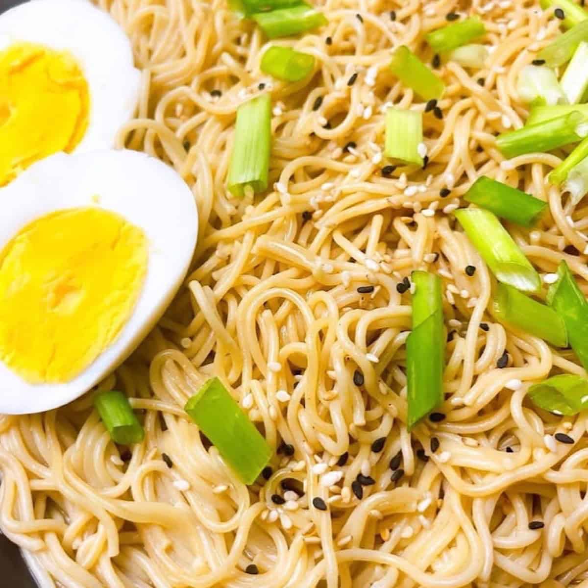 Garlic ginger ramen in a black bowl with sesame garnish and hard boiled eggs.