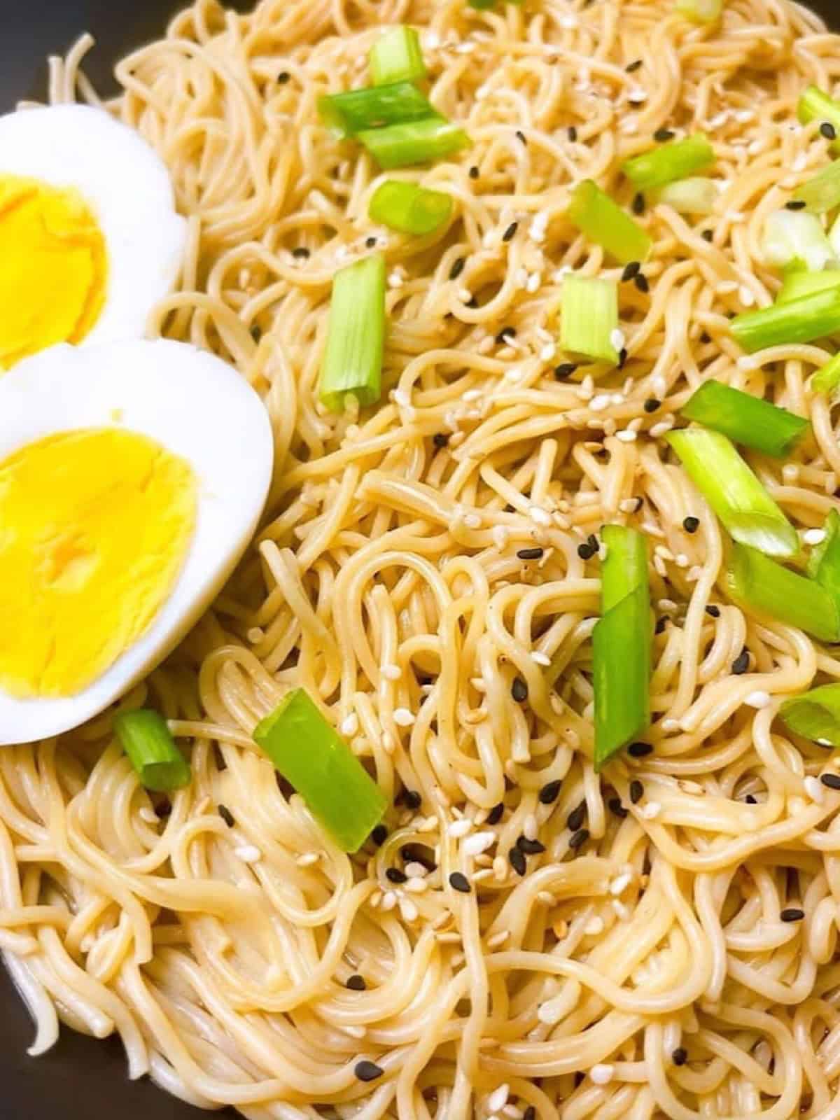 Garlic ginger ramen in a black bowl with sesame garnish and hard boiled eggs.