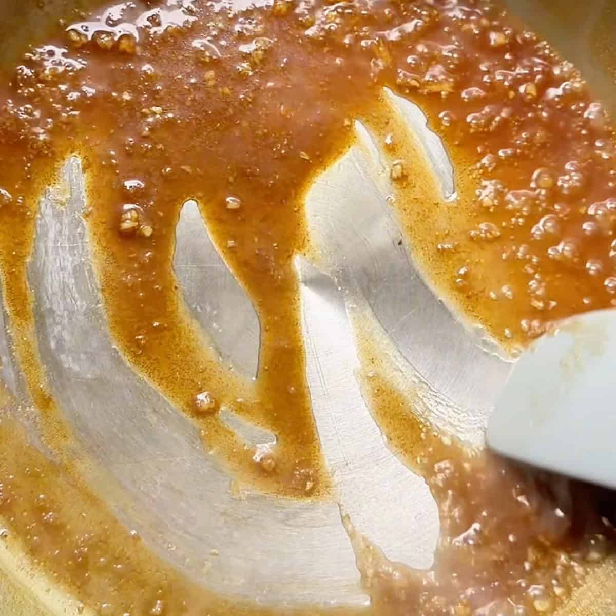 Rubber spatula running through the reduced garlic ginger sauce in a skillet.