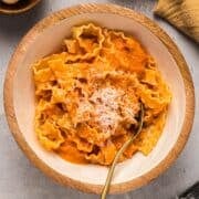 Homemade vodka sauce over pasta garnished with parmesan in a decorative wooden bowl.