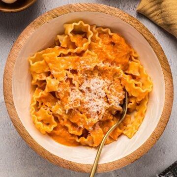 Homemade vodka sauce over pasta garnished with parmesan in a decorative wooden bowl.