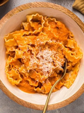 Homemade vodka sauce over pasta garnished with parmesan in a decorative wooden bowl.