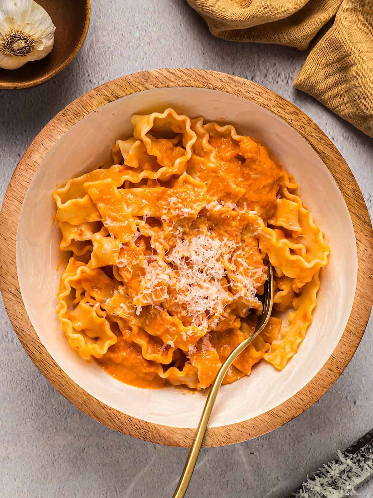 Homemade vodka sauce over pasta garnished with parmesan in a decorative wooden bowl.