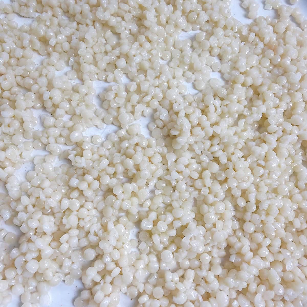 Tender cooked pearl couscous spread out on a plate.