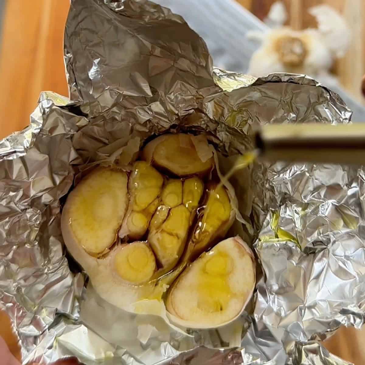 Drizzling oil over a garlic bulb with top removed.