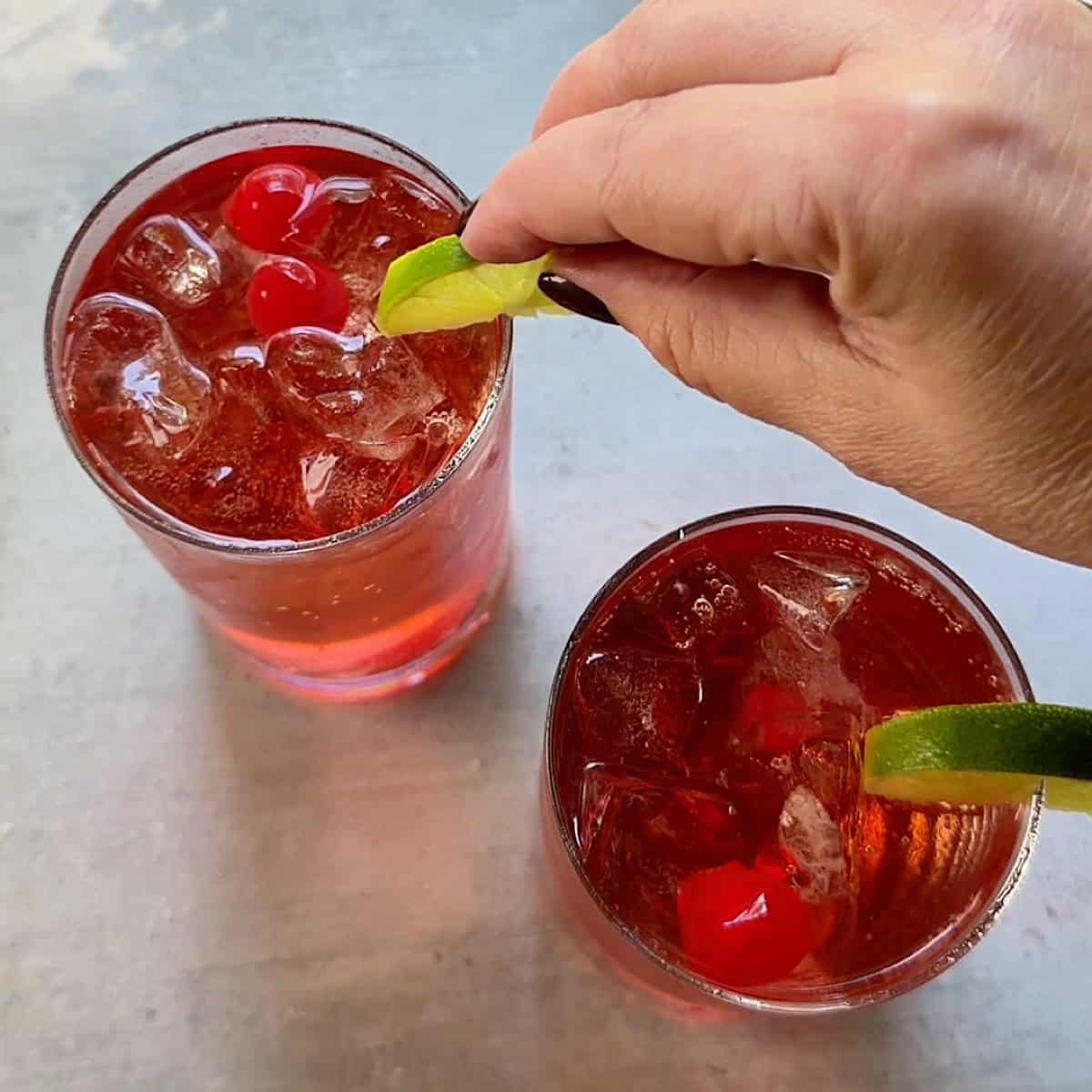 Garnishing glasses of shirley temple with lime wedges.