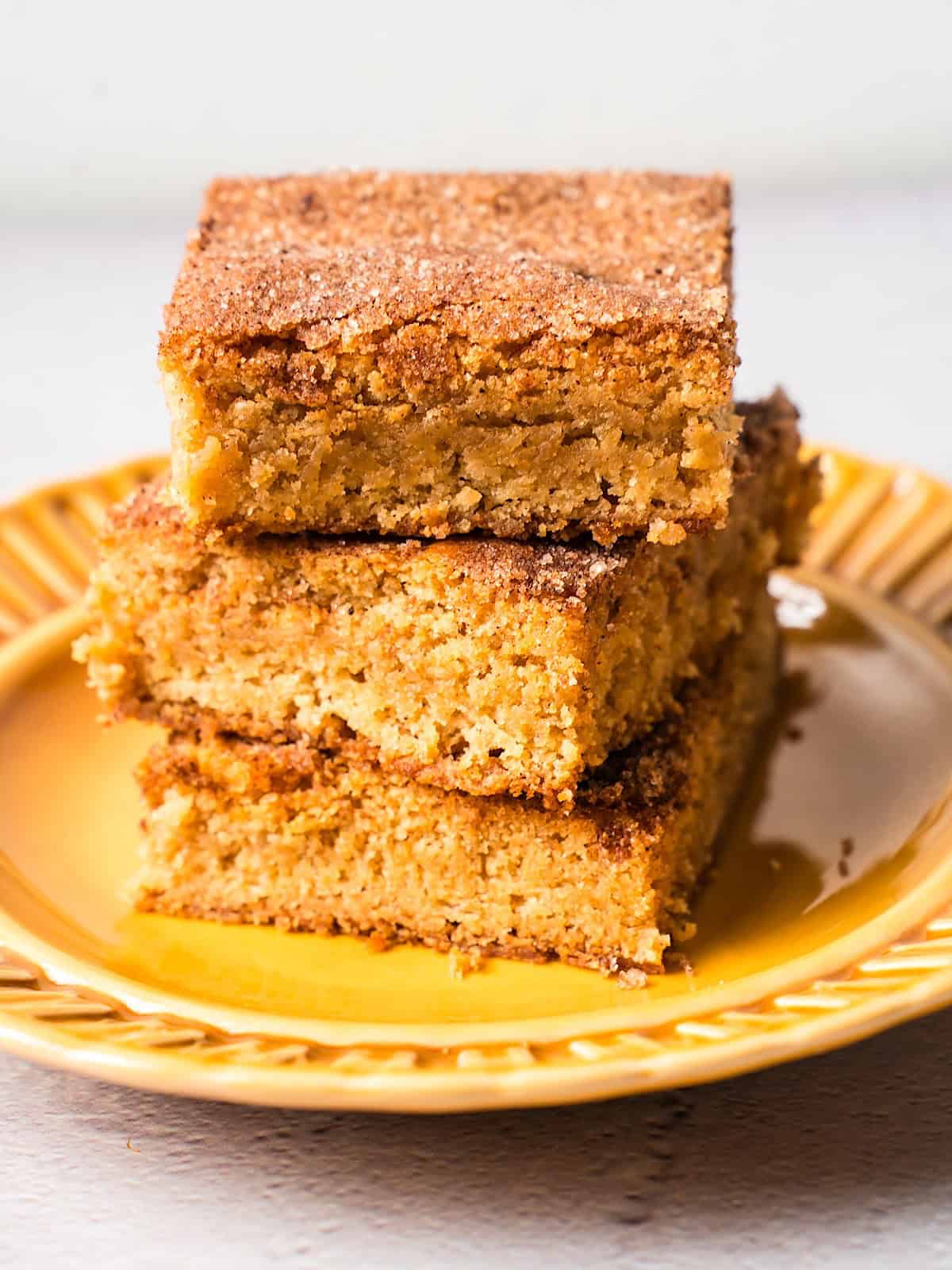 Three snickerdoodle blondies stacked high on a fall yellow decorative plate.