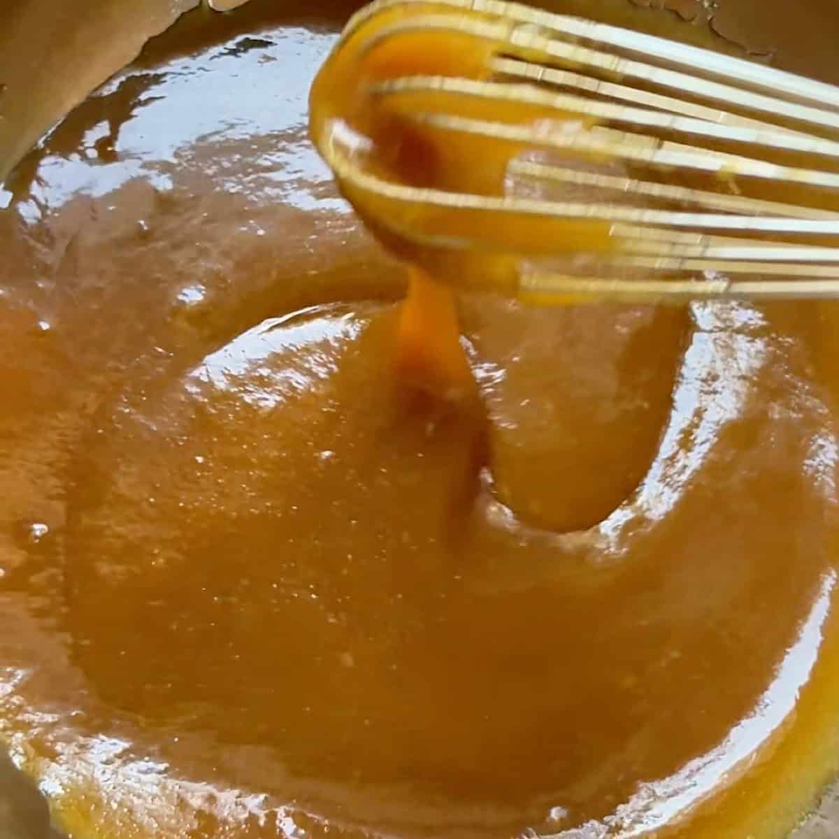 A whisk drizzling batter to show the consistency of the whisked wet ingredients.
