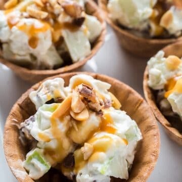 Four Snickers caramel apple salads in waffle bowls with peanut garnish.