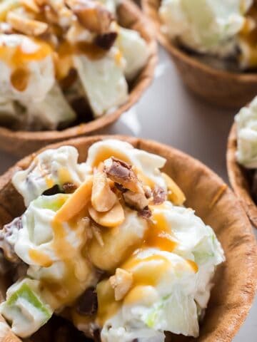 Four Snickers caramel apple salads in waffle bowls with peanut garnish.
