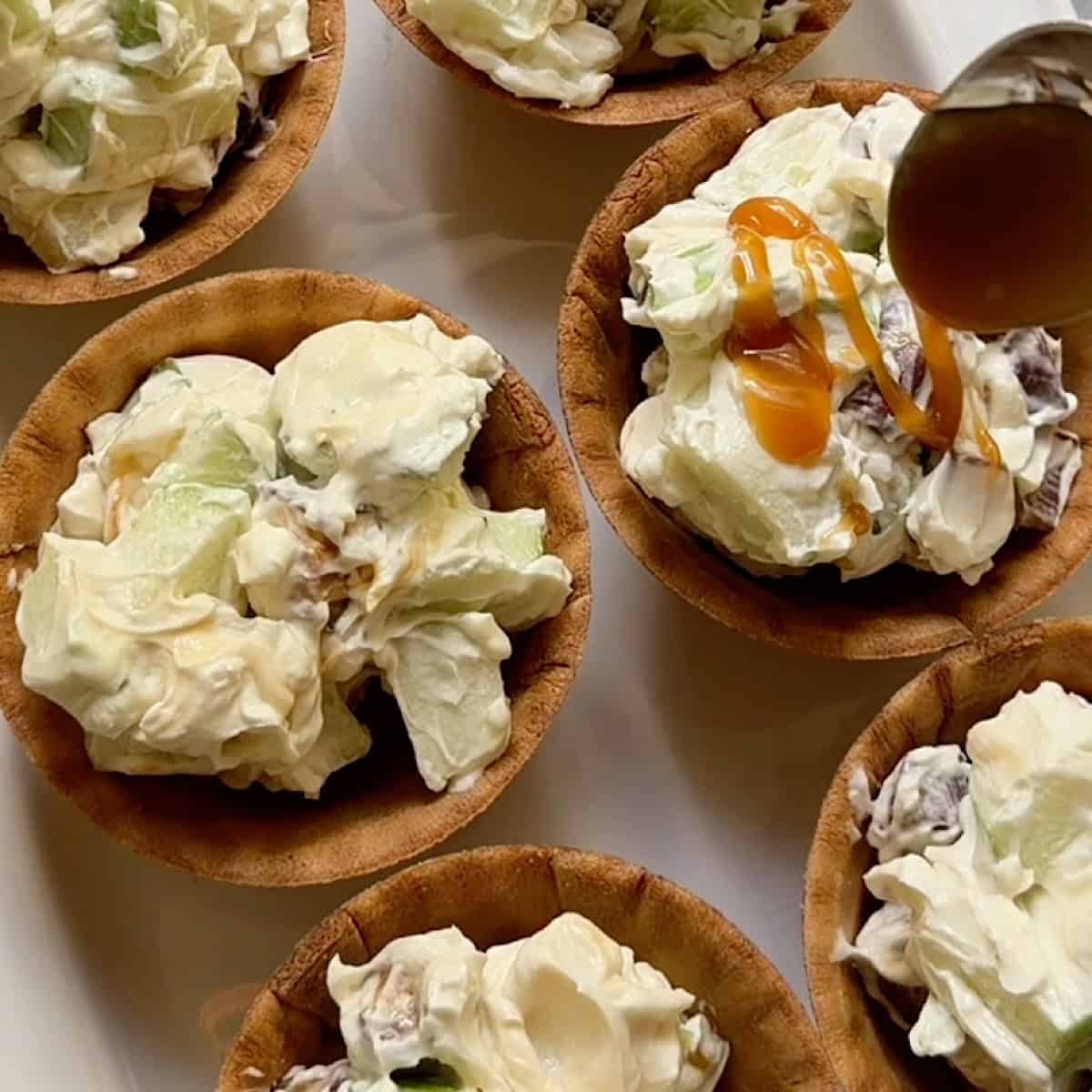Spooning caramel over waffle bowls full of Snickers and apple salad.